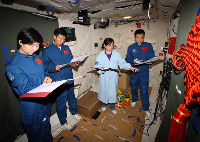 Тренер космонавтов тренирует экипаж космического корабля “Шэнчжоу-9” -- Цзин Хайпэн, Лю Ван и Лю Ян в космическом аппарате “Тяньгун-1”.