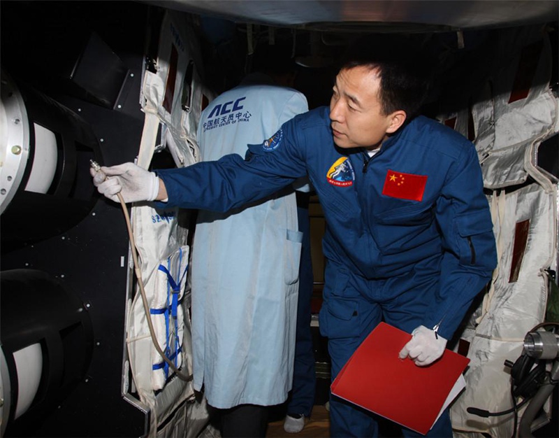 Цзин Хайпэн проверяет экспериментальное оборудование в космическом аппарате “Тяньгун-1”.